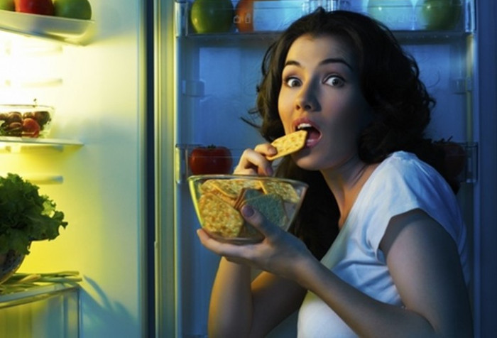 Žena ispred frižidera jede krekere u kasne sate